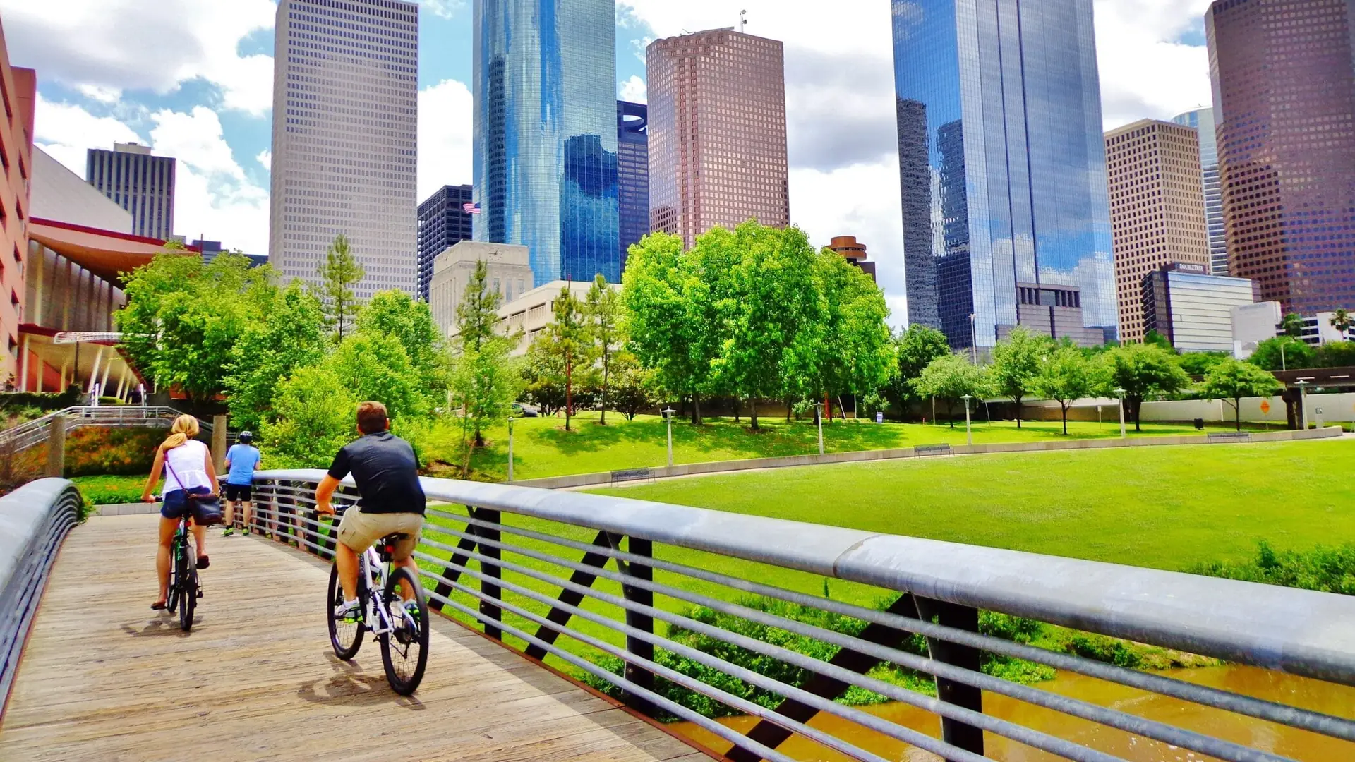 Cyclists crossing a Buffalo Bayou footbridge beneath the downtown Houston skyline